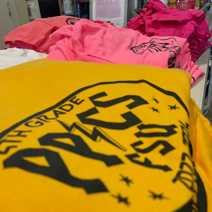 Stack of custom printed school event t-shirts in bright yellow and pink by Miami Epic Tees